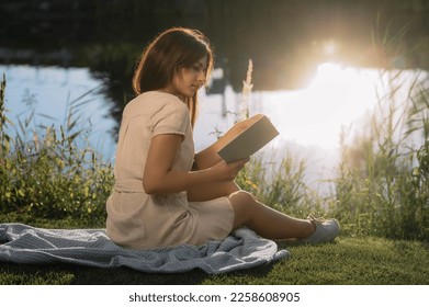 Young woman reading book near lake on sunny day - Shutterstock ID 2258608905