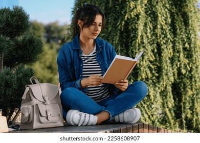 Young woman reading book on bench outdoors - Shutterstock ID 2258608907