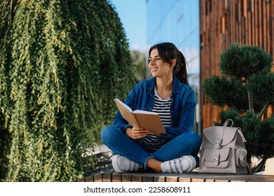 Young woman reading book on bench outdoors - Shutterstock ID 2258608911