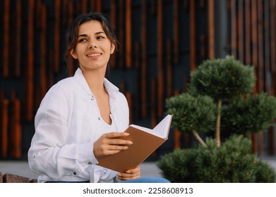Young woman reading book on bench outdoors - Shutterstock ID 2258608913