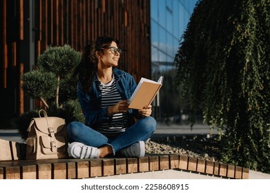 Young woman reading book on bench outdoors - Shutterstock ID 2258608915