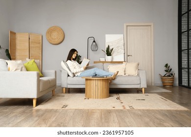 Young woman reading book on sofa in living room - Powered by Shutterstock