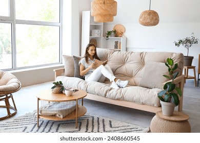 Young woman reading book on couch in living room - Powered by Shutterstock