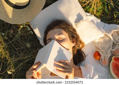 Young Woman Reading Book In Outdoor Field. Reading And Relaxation. Summer Time.