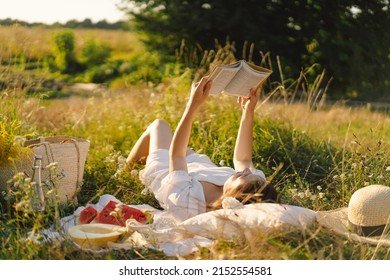 Young Woman Reading Book In Outdoor Field. Reading And Relaxation. Summer Time.