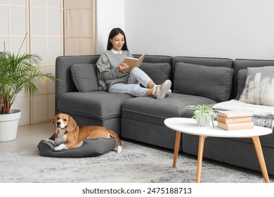 Young woman reading book and resting with cute Beagle dog on sofa in living room - Powered by Shutterstock