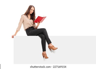 Young Woman Reading A Book Seated On A Panel Isolated On White Background