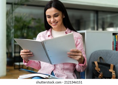 Young Woman Reading Book At Table In Library And Smiling Toothy. Brunette Lady Studying At The High School. Stock Photo 