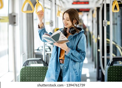 Young woman reading book while standing in the modern tram, happy passenger moving by comfortable public transport - Powered by Shutterstock