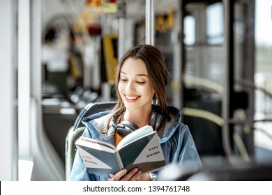 Young woman reading book while moving in the modern tram, happy passenger at the public transport - Powered by Shutterstock