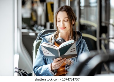 Young woman reading book while moving in the modern tram, happy passenger at the public transport - Powered by Shutterstock