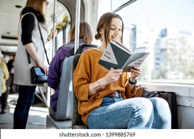 Young woman reading book while moving in the modern tram, happy passenger at the public transport - Powered by Shutterstock