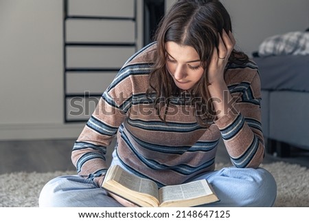A young woman is reading a book while sitting in her room on the floor, the concept of education and love of reading.
