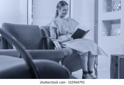 Young Woman Reading Brochure In Doctor's Waiting Room.