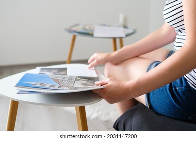 Young Woman Reading A Catalog Or Travel Magazine And Chooses A Destination To The Trip In A Beautiful Modern Living Room