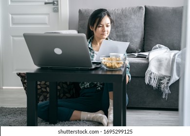 Young woman reading documents or reports while working on a laptop at home. Distance work or online education. Stay home while quarantined against coronavirus - Shutterstock ID 1695299125