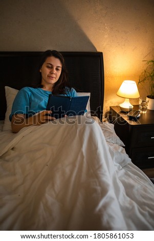 young woman reading electronic book with night light lamp