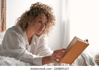 Young woman reading interesting book while relaxing on soft bed - Shutterstock ID 2208895127