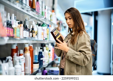 Young woman reading label on skin care product while shopping at the mall. - Powered by Shutterstock