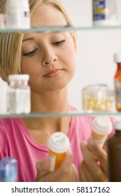 A Young Woman Is Reading The Labels Of To Medicine Containers From Her Medicine Cabinet.  Vertical Shot.