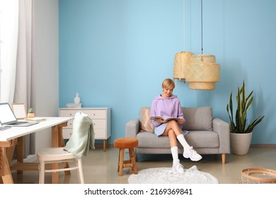 Young woman reading magazine on comfortable sofa near blue wall - Powered by Shutterstock