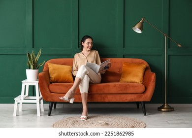 Young woman reading magazine on red sofa near green wall - Shutterstock ID 2251862985