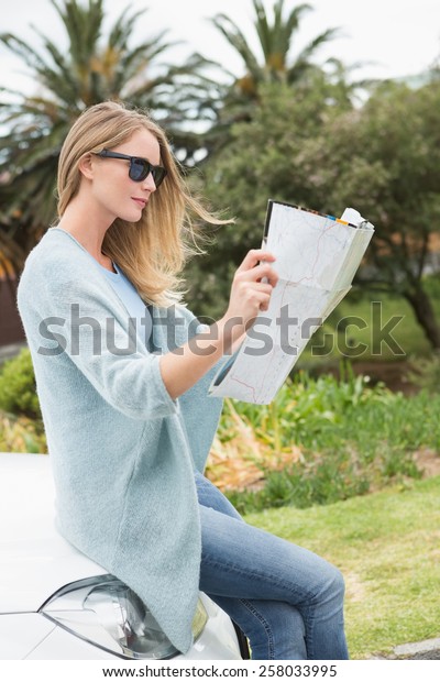 Young woman reading a\
map beside her car