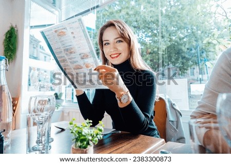 Young woman reading menu sitting with friend at casual cafe. Smiling woman checking menu, choosing meal or drink, making order. Try new foods while traveling. real people. copy space. Selective focus