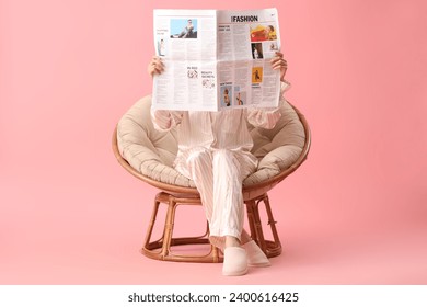Young woman reading newspaper in armchair on pink background - Powered by Shutterstock