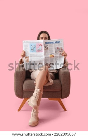 Young woman reading newspaper in soft armchair on pink background