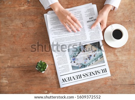 Young woman reading newspaper at table