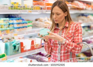 Young Woman Reading Nutrition Label On Diary Food In Local Supermarket.