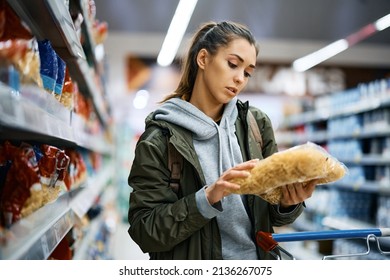 Young Woman Reading Nutrition Label While Buying Pasta At Supermarket.