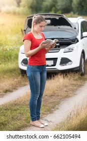 Young Woman Reading Owner Manual At Broken Car In Meadow