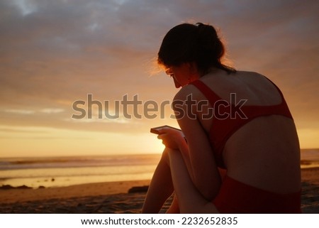 Young woman reading a tablet on a beach at sunset wearing a red bikini with beautiful clouds