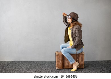 Young woman is ready to travel. Funny woman sitting on retro suitcase against concrete wall background. Summer vacation during pandemic coronavirus concept