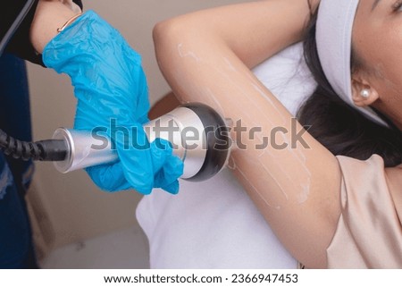 A young woman receives a radiofrequency upper arm skin tightening or slimming treatment. At a facial care, dermatologist or aesthetic clinic.