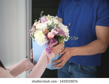 Young Woman Receiving Beautiful Flowers From Delivery Man At Home