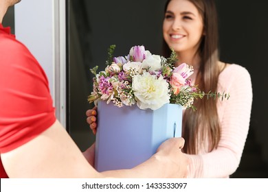 Young Woman Receiving Beautiful Flowers From Delivery Man At Home