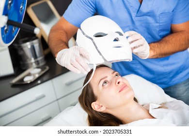 Young Woman Receiving Face Light Therapy In LED Mask In Aesthetic Medicine Office.