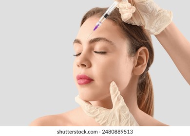 Young woman receiving filler injection in forehead on grey background - Powered by Shutterstock