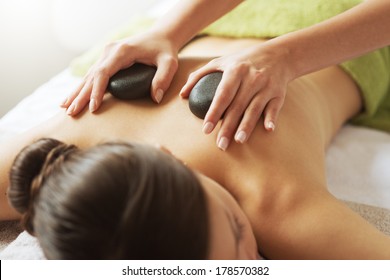 Young Woman Receiving A Hot Stone Massage Therapy At Spa.