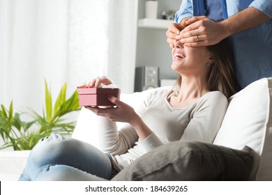 Young Woman Receiving A Surprise Gift Box From Her Boyfriend At Home.