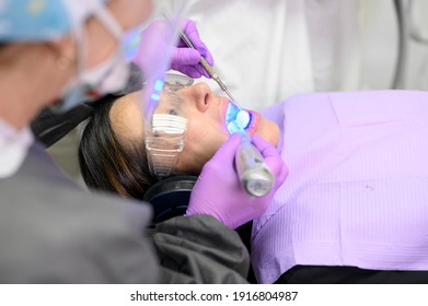 Young Woman Receiving Ultraviolet Light For Whitening Procedure At Dentist Office. High Quality Photo