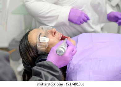 Young Woman Receiving Ultraviolet Light For Whitening Procedure At Dentist Office. High Quality Photo