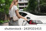 Young woman recharge EV electric car battery at residential area EV charging station in urban city condo with sustainable green and renewable clean energy lifestyle for electric vehicle innards