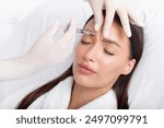 Young woman recieving injection of anti-aging botox filler to forehead from professional cosmetologist in beauty salon