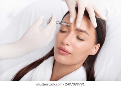 Young woman recieving injection of anti-aging botox filler to forehead from professional cosmetologist in beauty salon