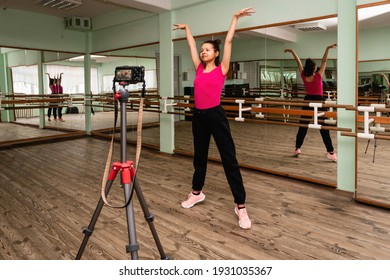 Young Woman Recording On Camera A Dance Lesson In A Choreography Hall With Mirrors. Fitness Trainer Shows A Warm-up Exercise