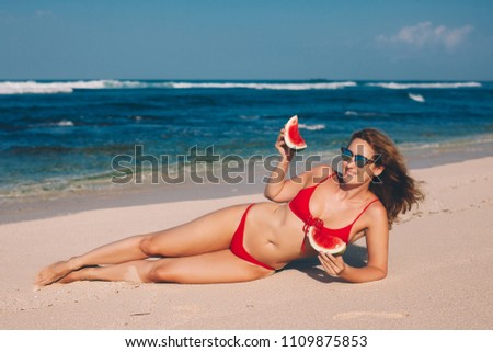 Young woman in red bikini with watermelon on the beach during her tropical vacation travel